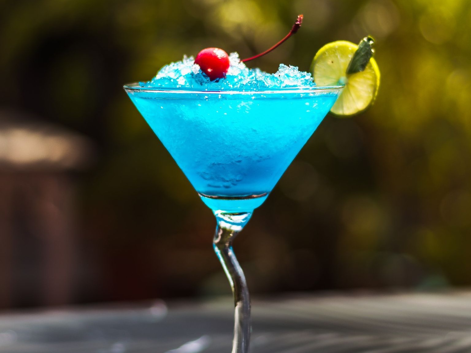 a blue cocktail garnished with a cherry and lime