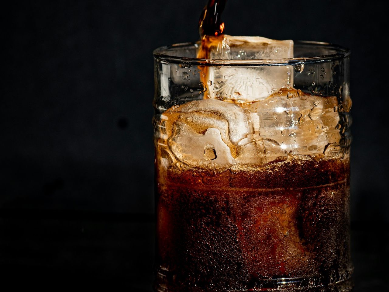 a glass filled with ice and coke on a table